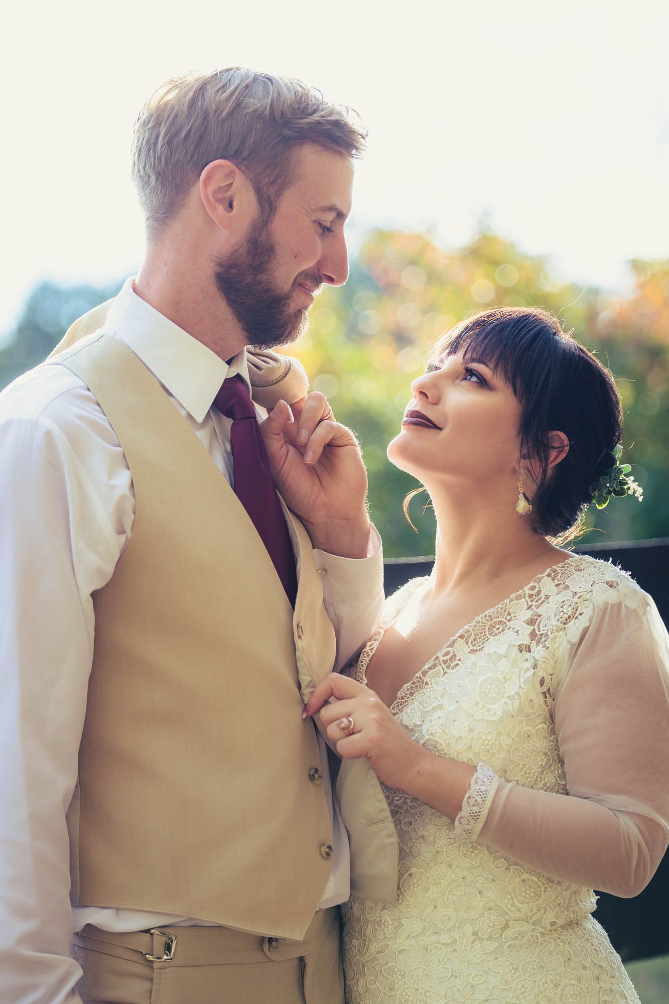 A bride and groom are standing next to each other and the bride is fixing the groom 's tie.