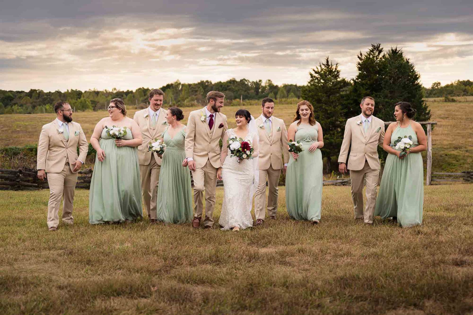 A bride and groom are walking with their wedding party in a field.
