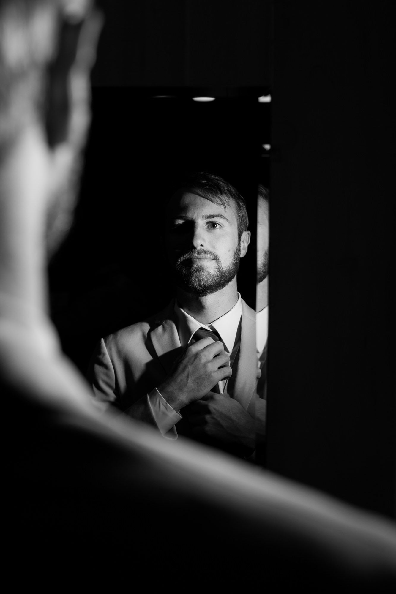 A man in a suit is adjusting his tie in front of a mirror.