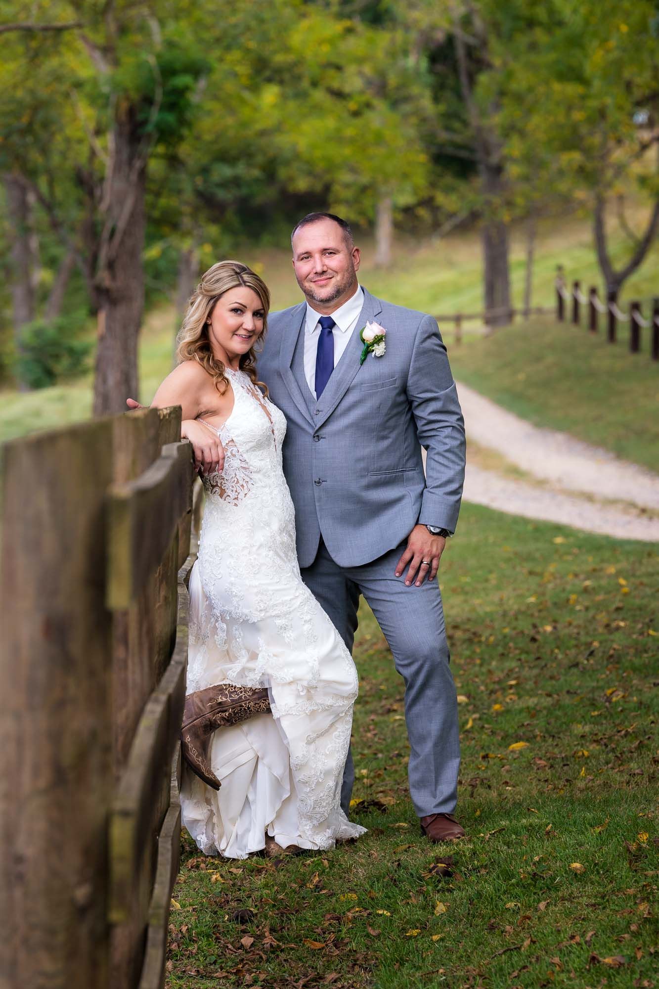 A bride and groom are posing for a picture next to a wooden fence.