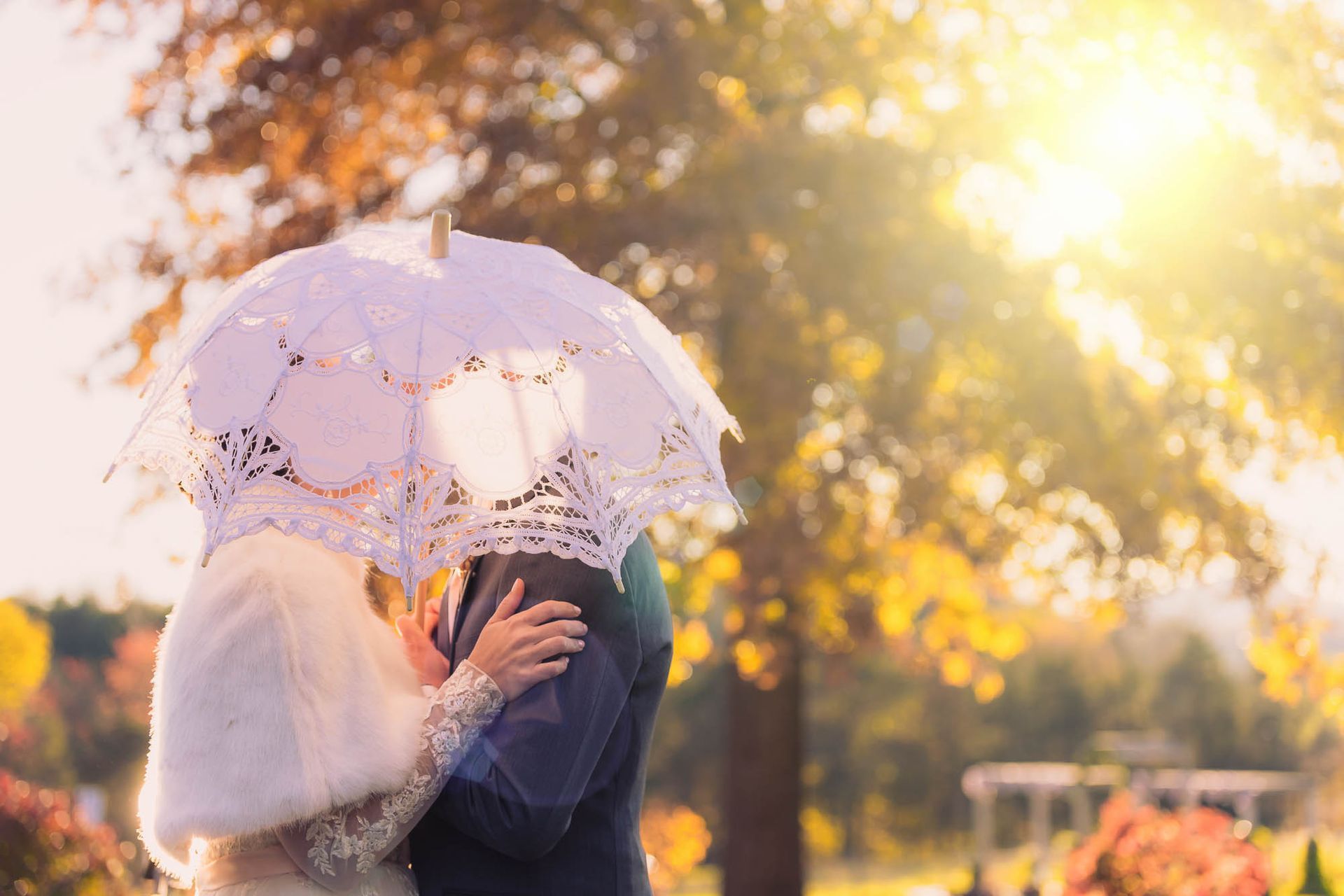A bride and groom are kissing under an umbrella in a park.