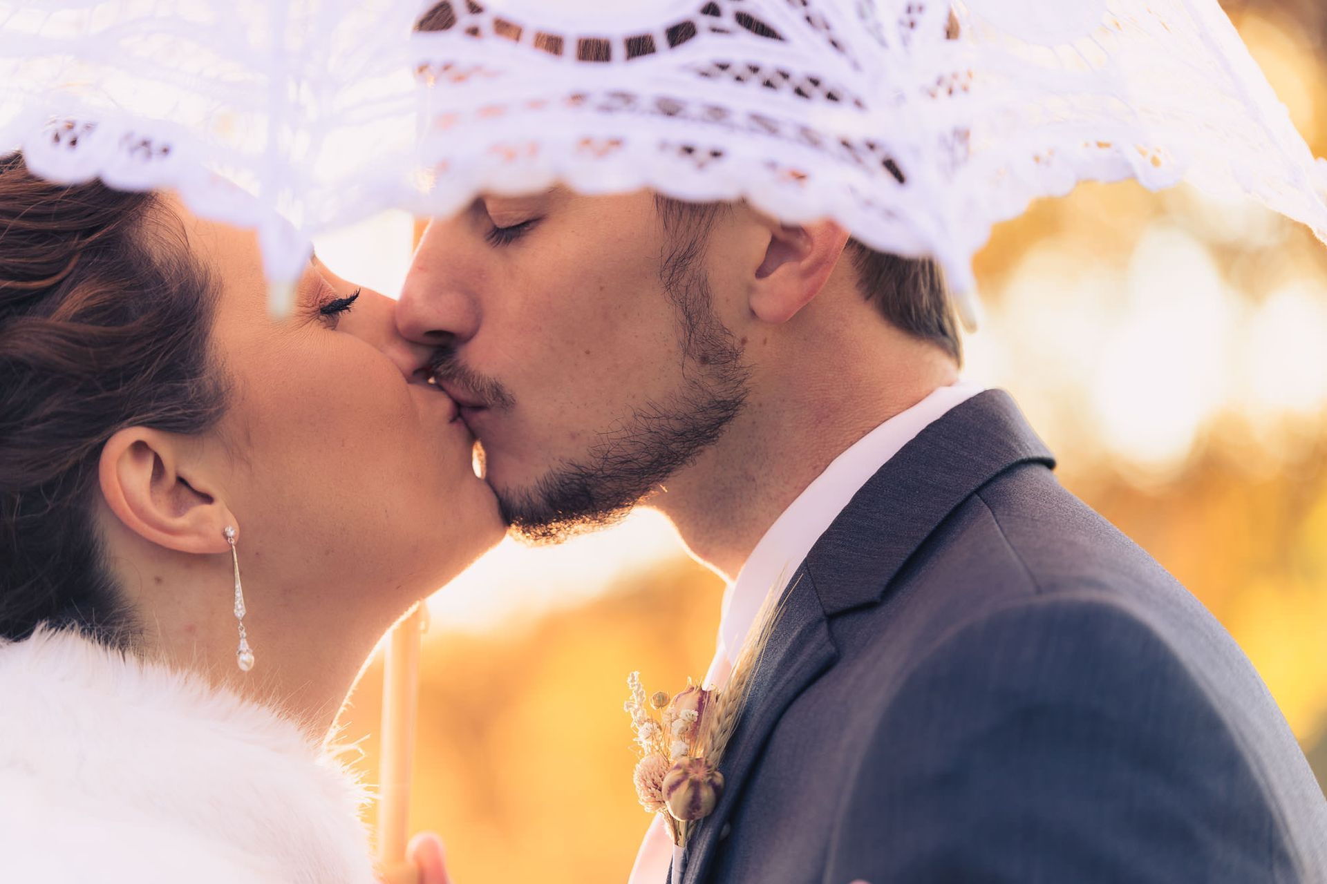 A bride and groom are kissing under an umbrella.
