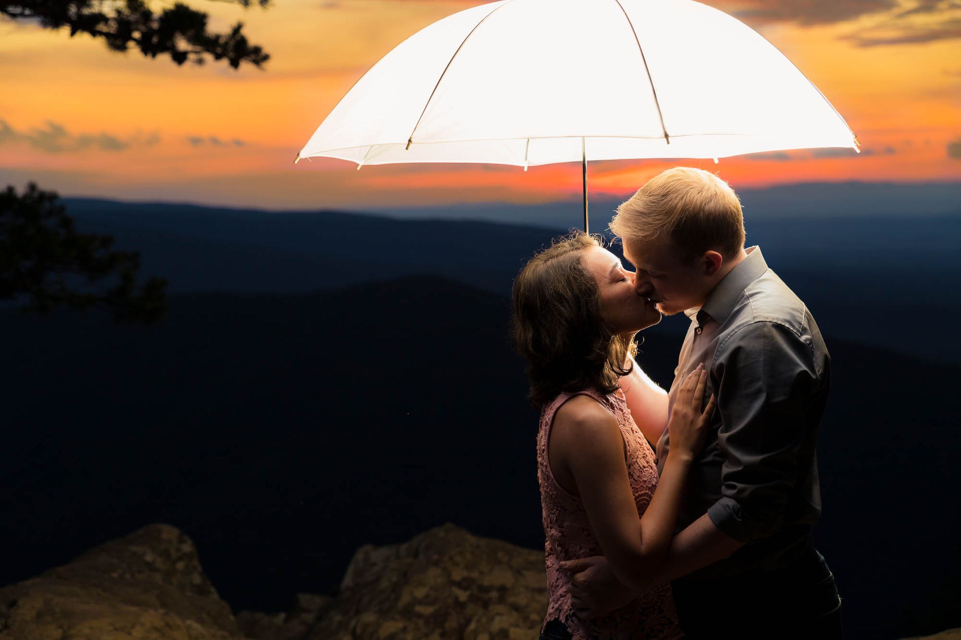 A man and a woman are kissing under an umbrella.
