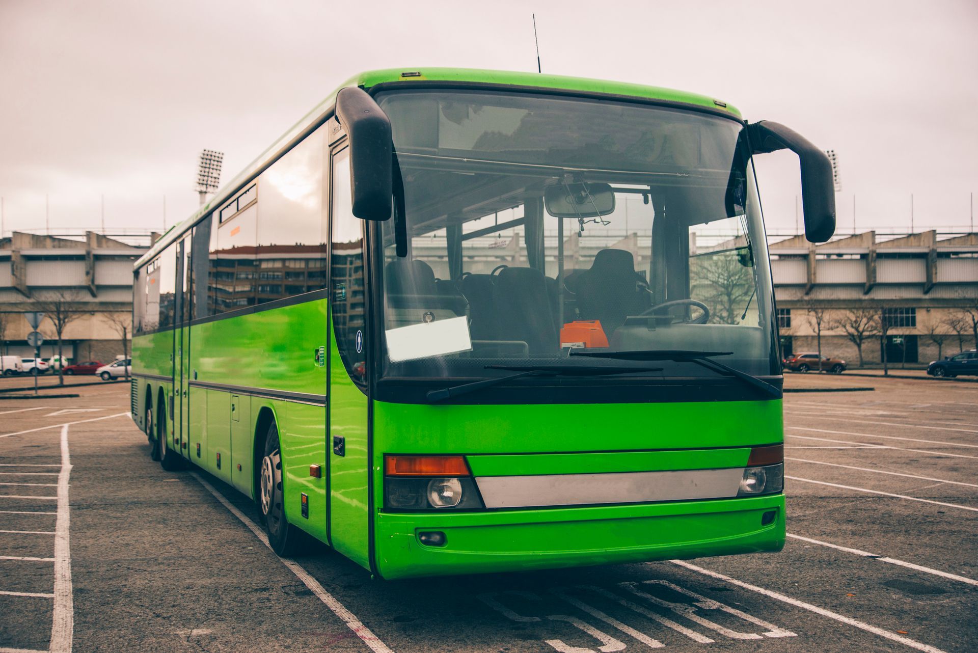 A green bus is parked in a parking lot.