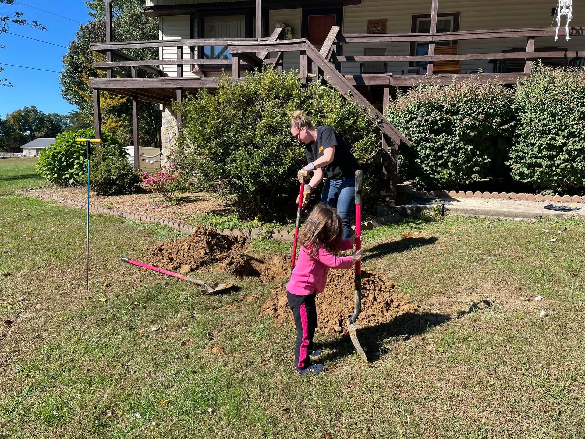A man and a little girl are digging a hole in the ground in front of a house.