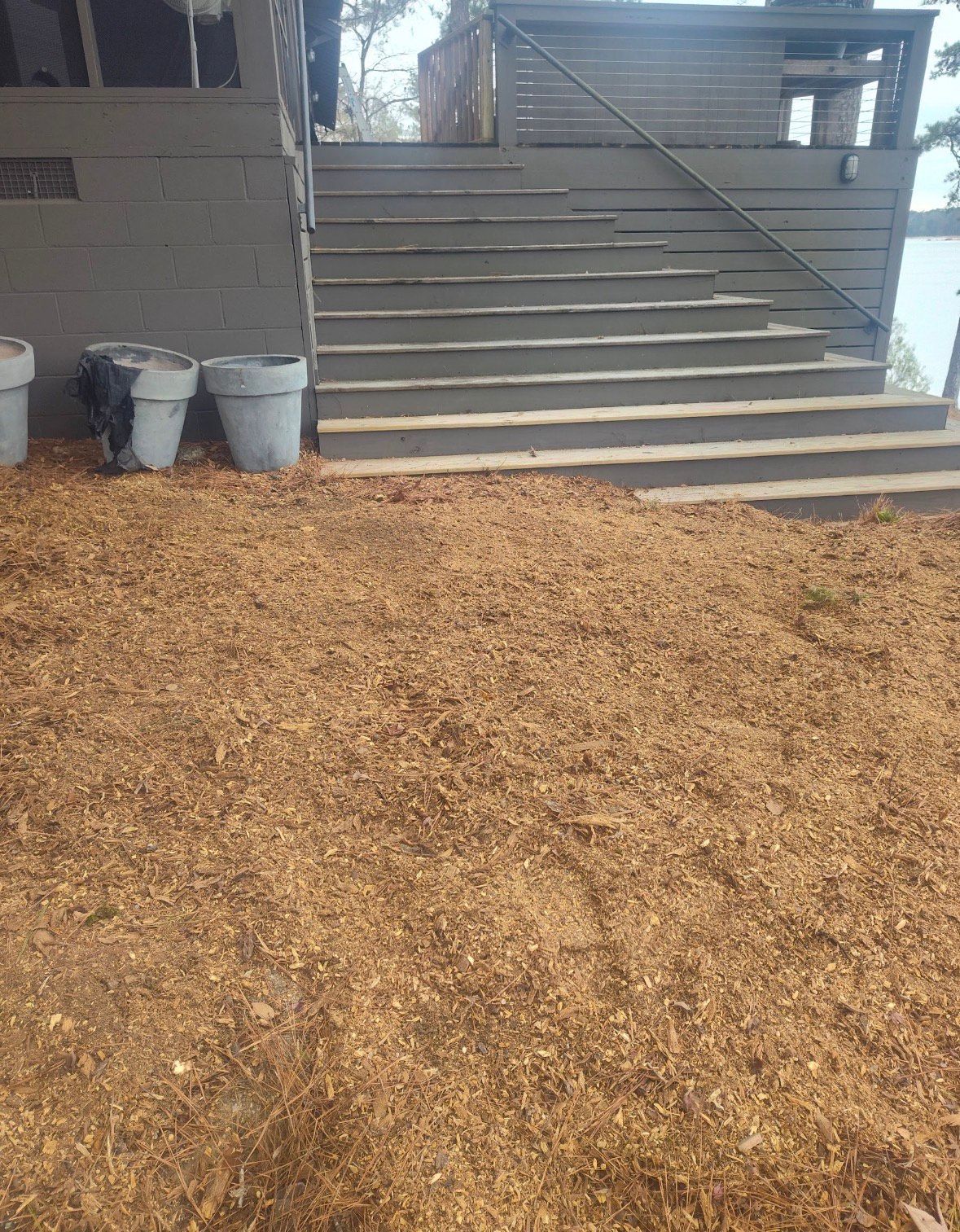 Mulched ground in front of gray steps leading up to a wooden structure, with potted plants on the left.