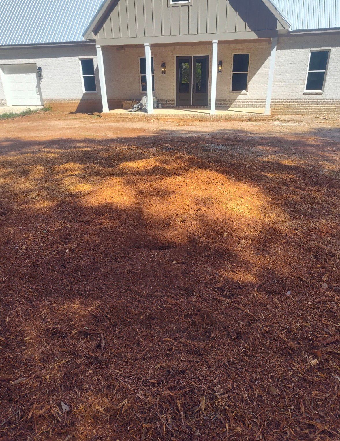 Front view of a house with a covered porch; the yard is covered in pine needles.
