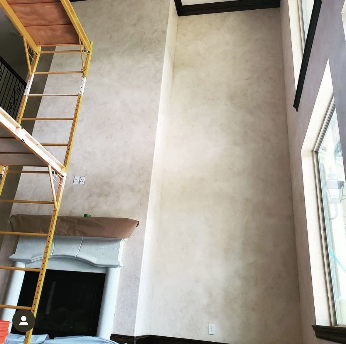 Interior with scaffolding near fireplace, beige wall finish, high ceiling, and window.
