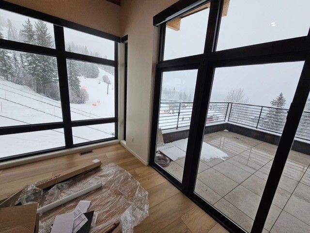 Interior view with large windows overlooking a snowy ski resort. Room has wood floors and cardboard boxes.