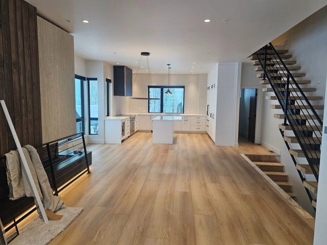 Modern open-plan kitchen with wood floors, white cabinets, island, and staircase.