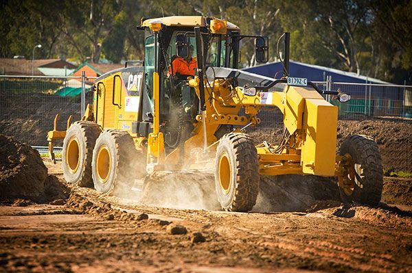 A man is driving a yellow tractor on a dirt road.