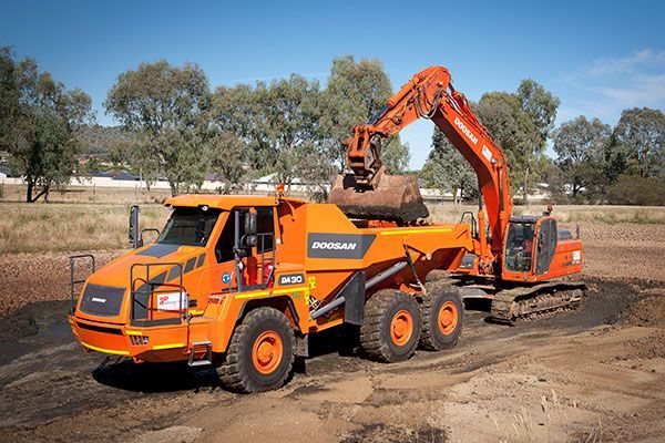 A dump truck is being towed by an excavator in a dirt field.
