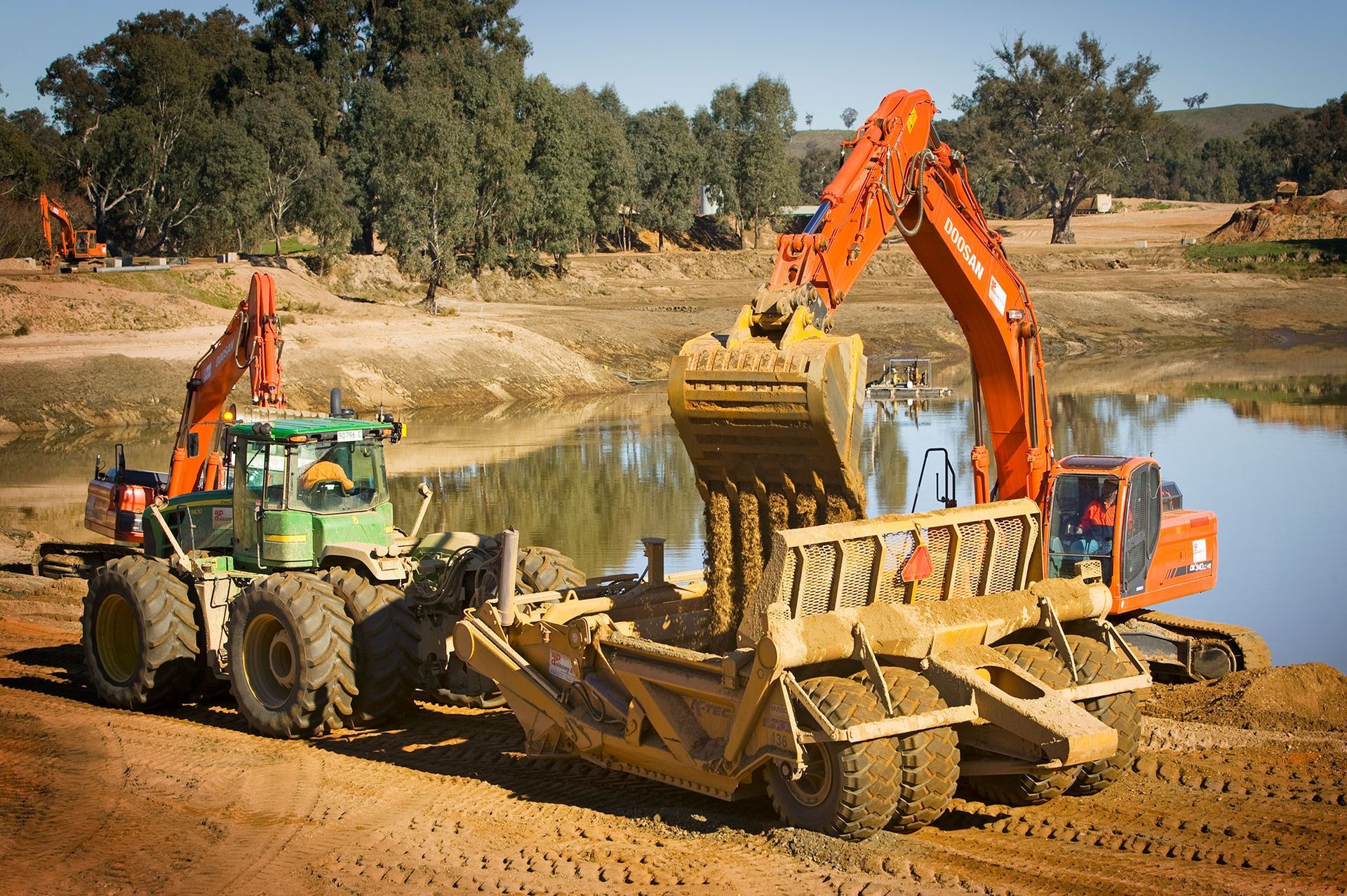 A bulldozer is being towed by a green tractor and an orange excavator.