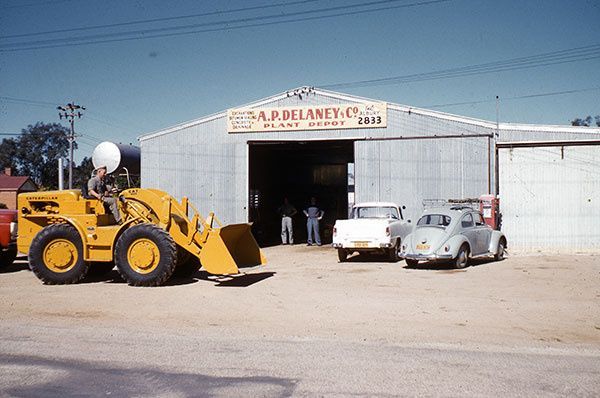 A yellow bulldozer is parked in front of a building that says s.a.p. bellamy co.
