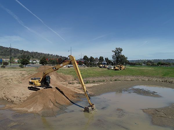 A large yellow excavator is digging in a muddy pond.