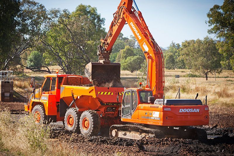 A doosan excavator is loading dirt into a dump truck