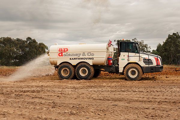A white truck is spraying dust on a dirt field.