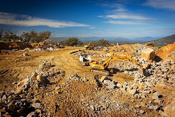 A construction site with a lot of rocks and dirt and a yellow excavator.