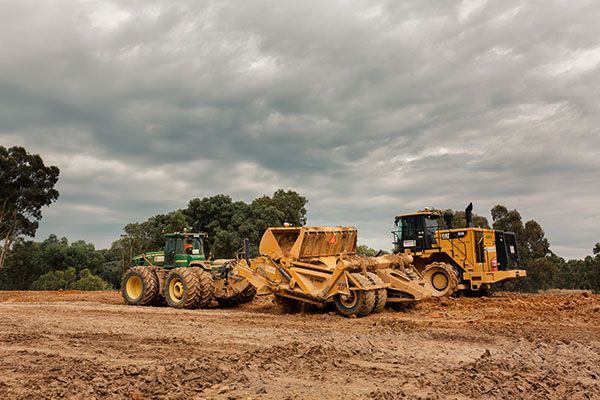 Two bulldozers are parked next to each other in a dirt field.