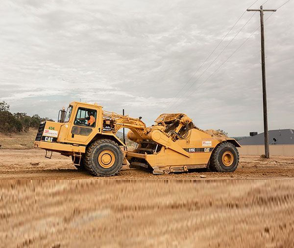 A yellow bulldozer is driving through a dirt field.