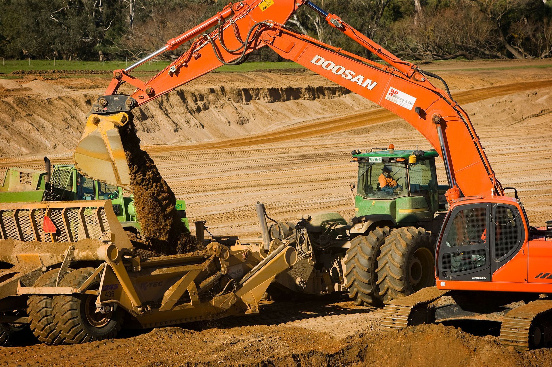 A doosan excavator is loading dirt into a bulldozer.