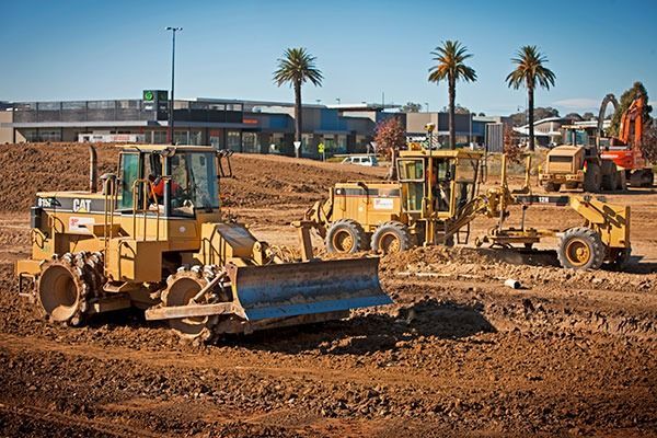 A group of construction vehicles are working on a dirt field.