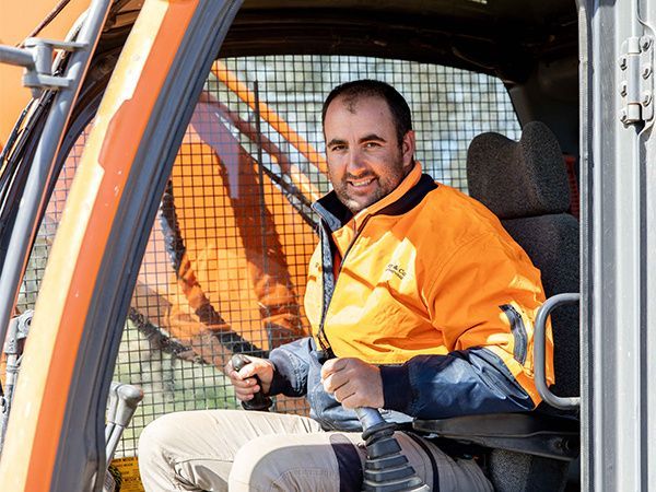 A man in an orange jacket is sitting in the driver 's seat of an excavator.