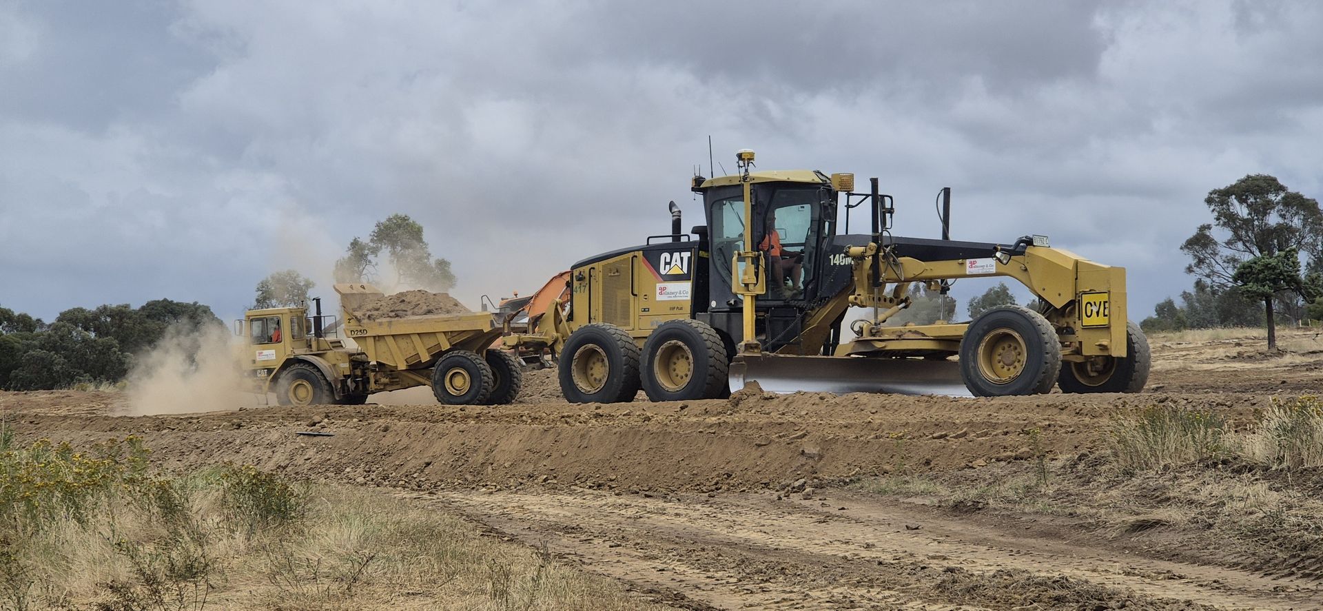 A dump truck is driving down a dirt road next to a trailer.