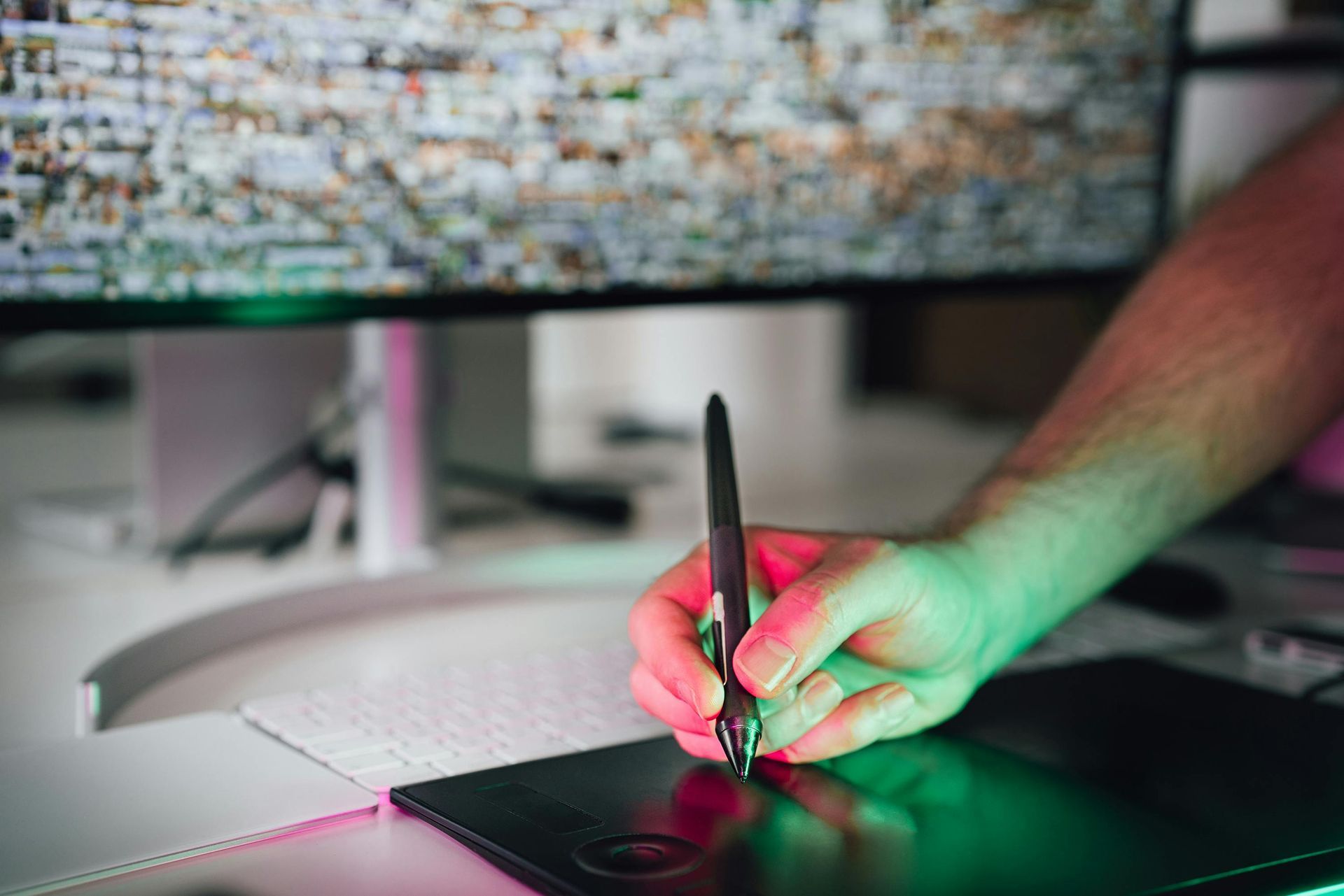 Hand using a stylus on a graphics tablet in front of a computer monitor with colorful lights