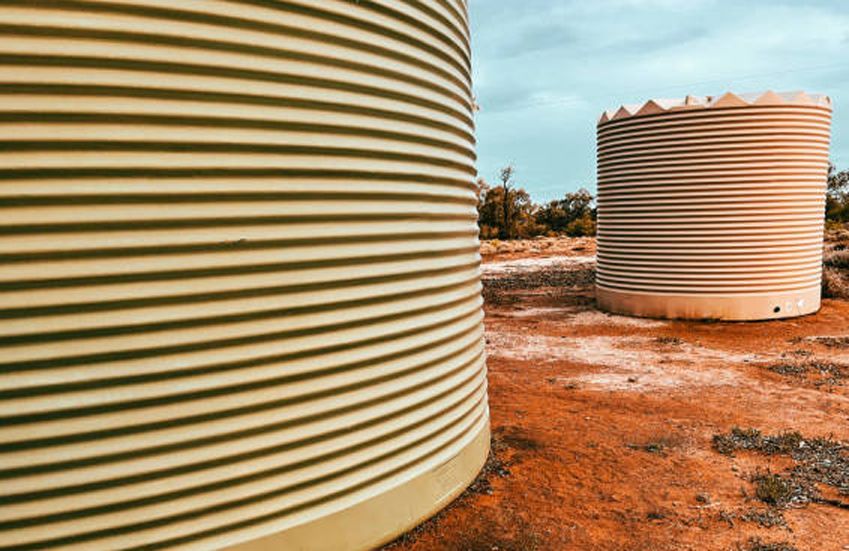 Two corrugated, cylindrical water tanks on red dirt under a blue sky.