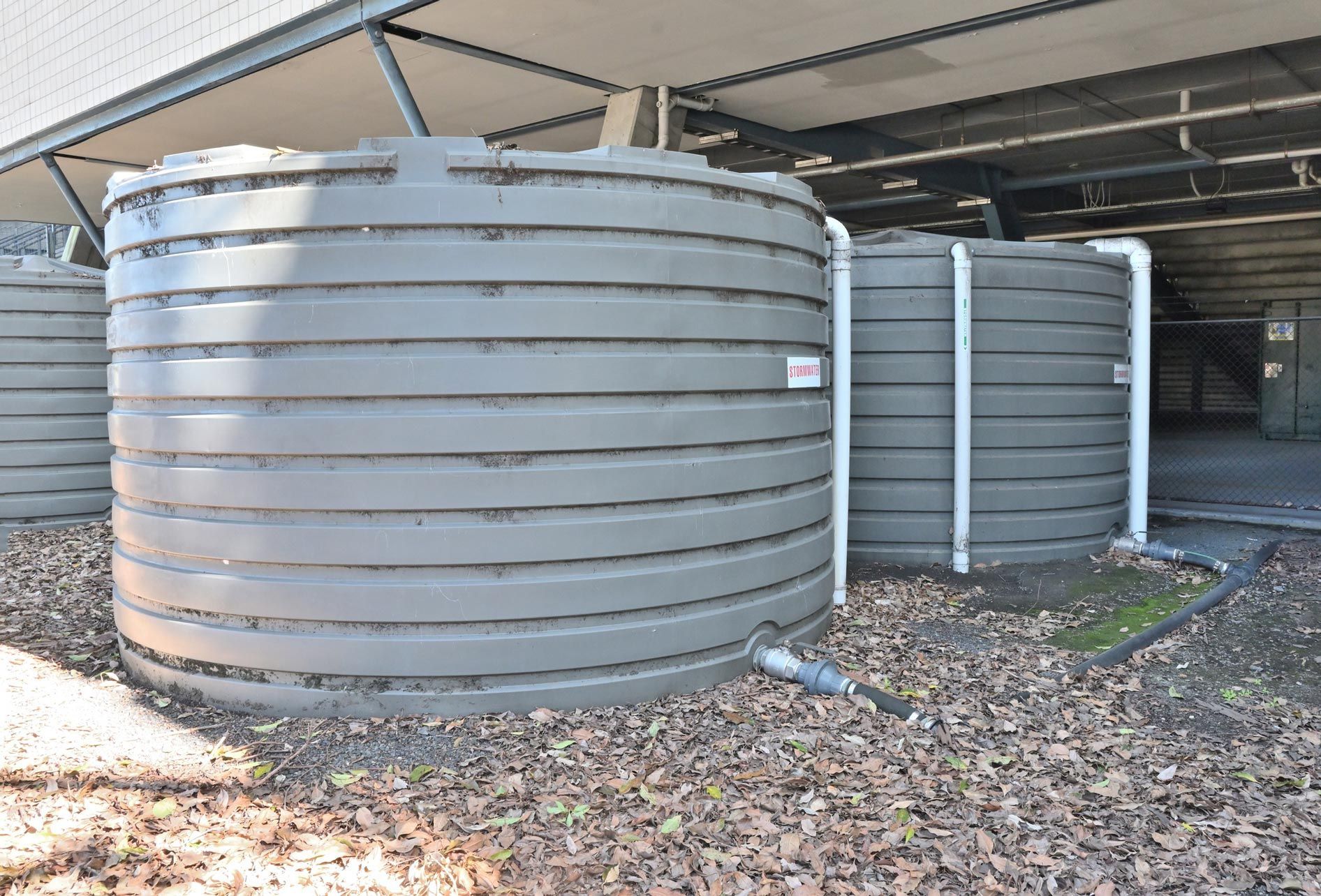 Three large, dark-gray, ribbed water tanks beneath a covered area.