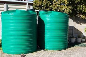 Two large, green, ribbed plastic water tanks in a backyard setting.