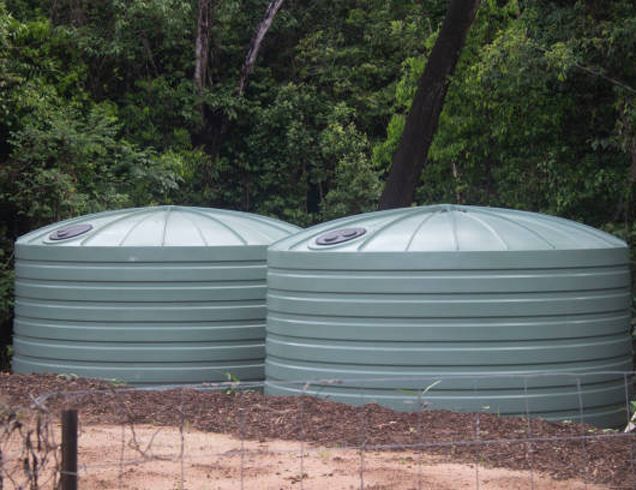 Two green, cylindrical water tanks with domed lids sit in a wooded area.