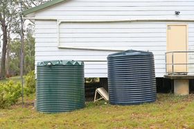Two corrugated metal water tanks, one green, one blue, next to a white house with a beige door. Two corrugated metal water tanks, one green, one blue, next to a white house with a beige door.