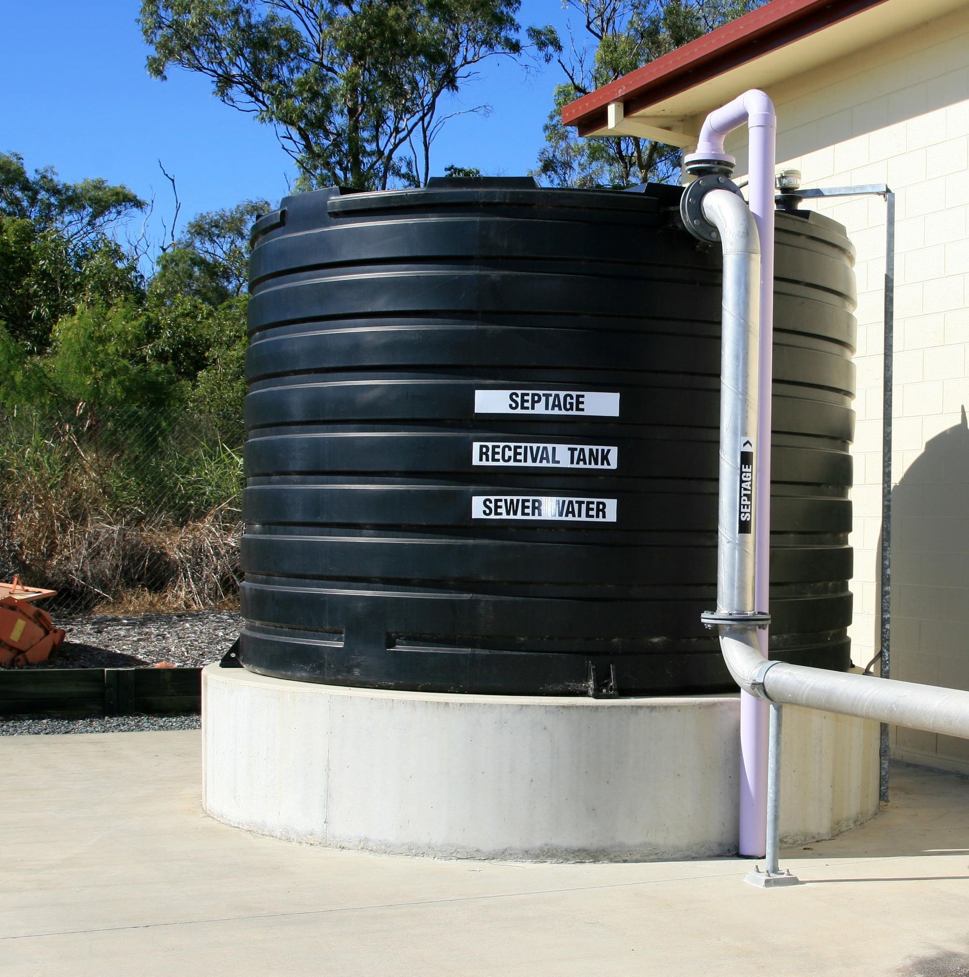 Black septic tank labeled 'Septage', 'Recital Tank', 'Sewer Water', against a building, pipes attached.