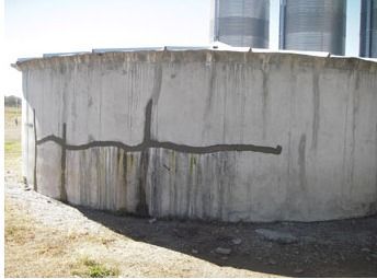 Cracked concrete silo with repaired horizontal and vertical cracks. Water stains are present.