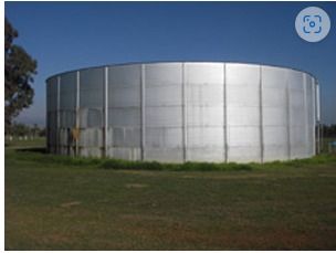 Large cylindrical water tank on a grassy field under a blue sky.
