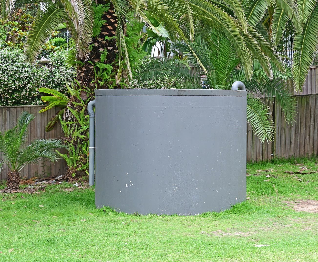 Gray circular water tank in a grassy yard, with a tree in the background.