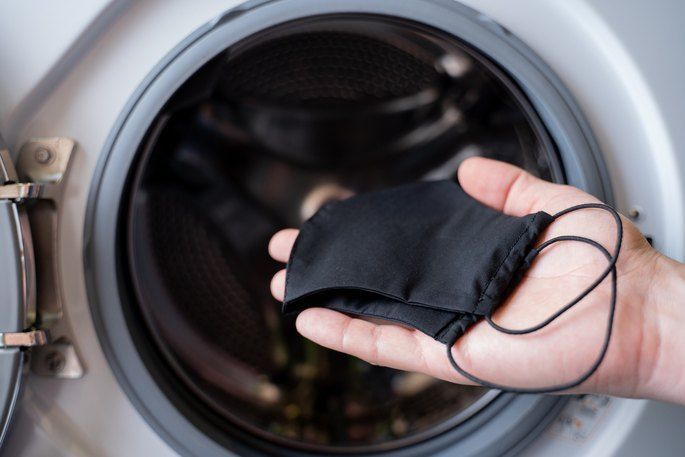 A person is putting a black face mask into a washing machine.