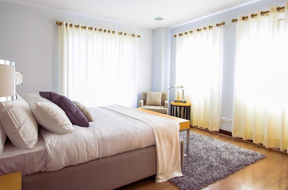 A bedroom with a bed , chair , rug and curtains.