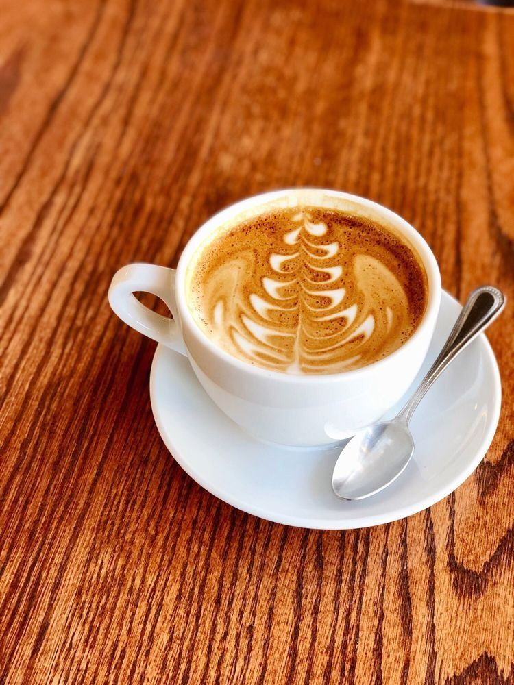 A cup of cappuccino on a saucer with a spoon on a wooden table.