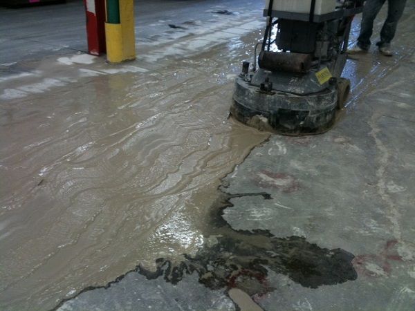 A mason using a level and screed to smooth and level a concrete floor base.