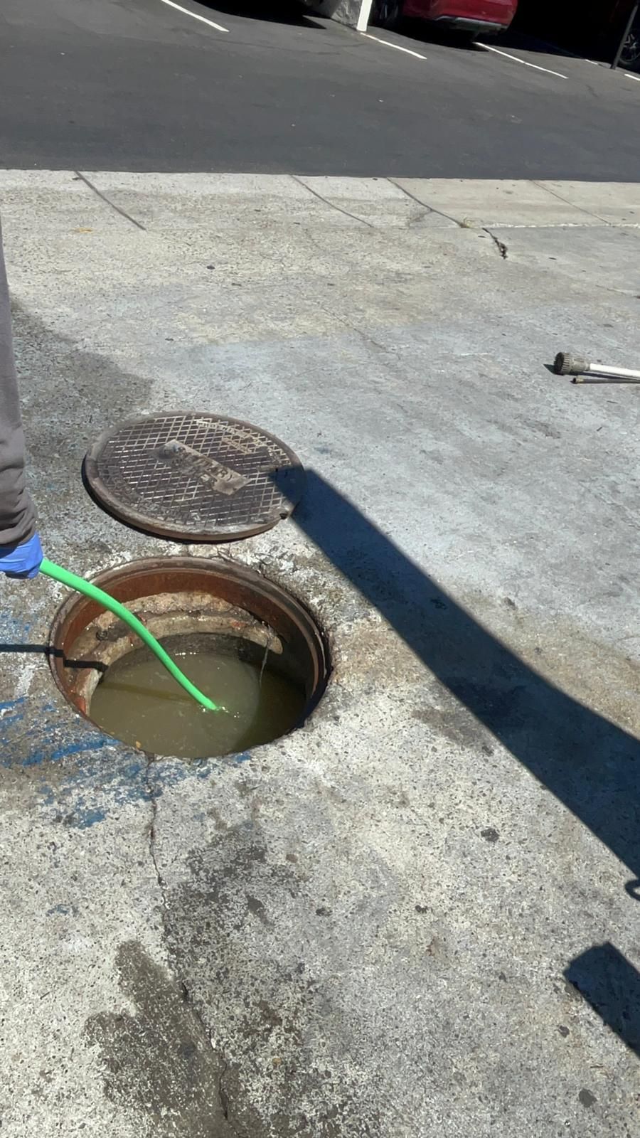 Manhole open on the street with a green hose inside, likely sewer work.