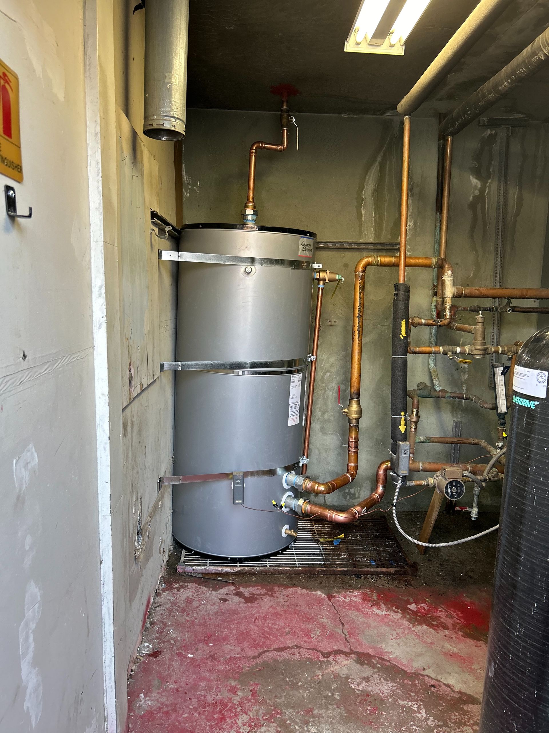 A man is working on a water heater while holding a clipboard.