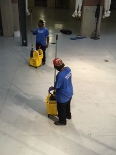 A man in a blue shirt is cleaning the floor with a mop and bucket.