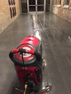 A red and black machine is cleaning the floor of a building.
