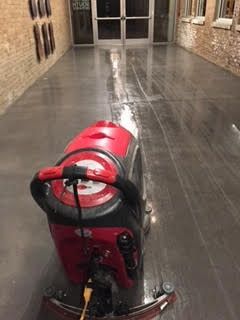 A red and black machine is cleaning a concrete floor in a building.