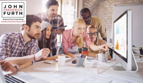 Team of six people looking at a computer screen with graphs in a bright office.