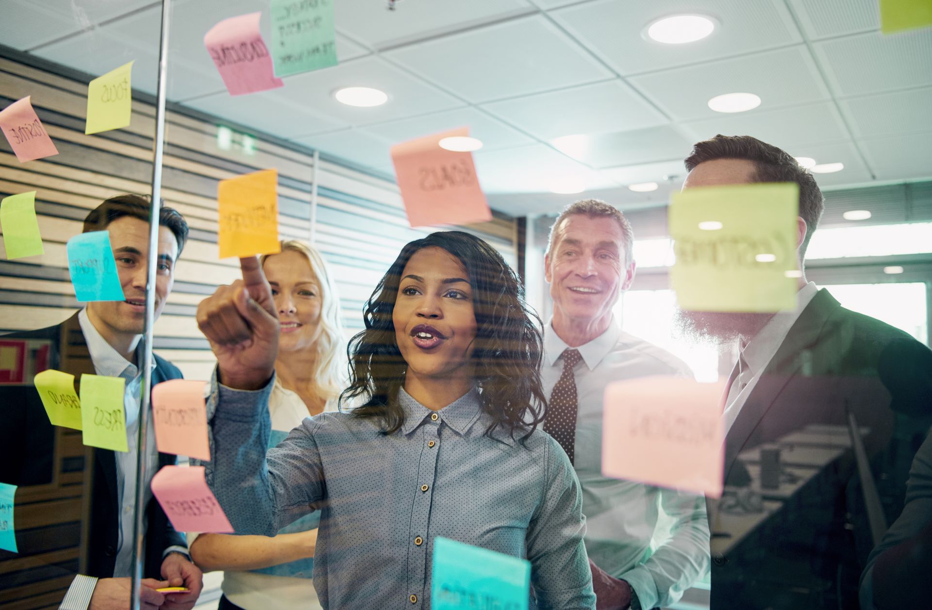Team in a meeting, brainstorming with sticky notes on a glass wall in an office. Team in a meeting, brainstorming with sticky notes on a glass wall in an office.