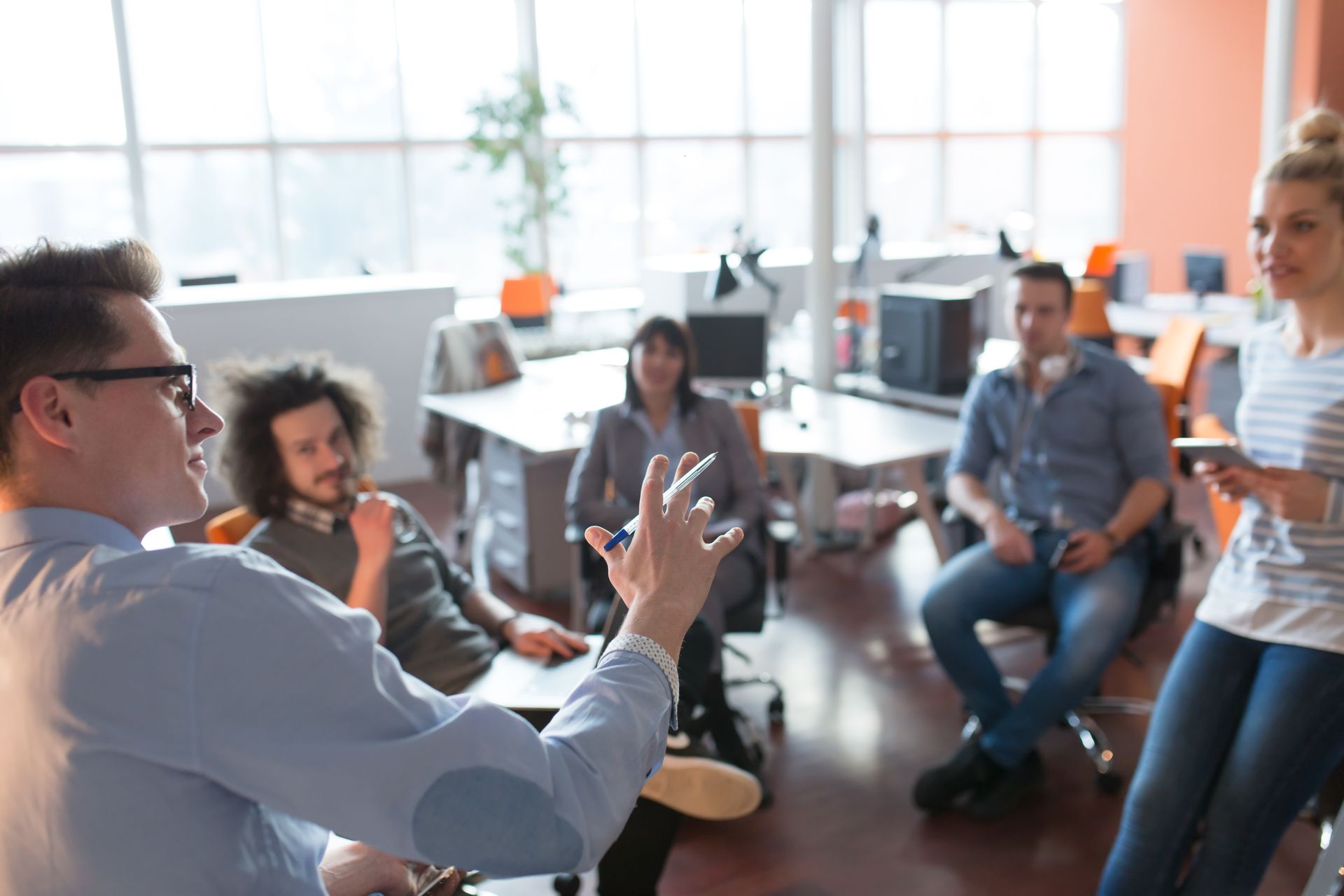 Man speaking to a group in an office; others listen and look on. Man speaking to a group in an office; others listen and look on.